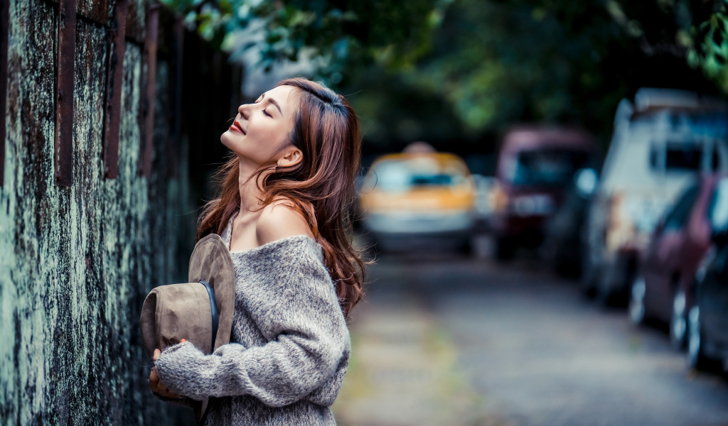 Девушка азиатка в теплом свитере стоит у забора