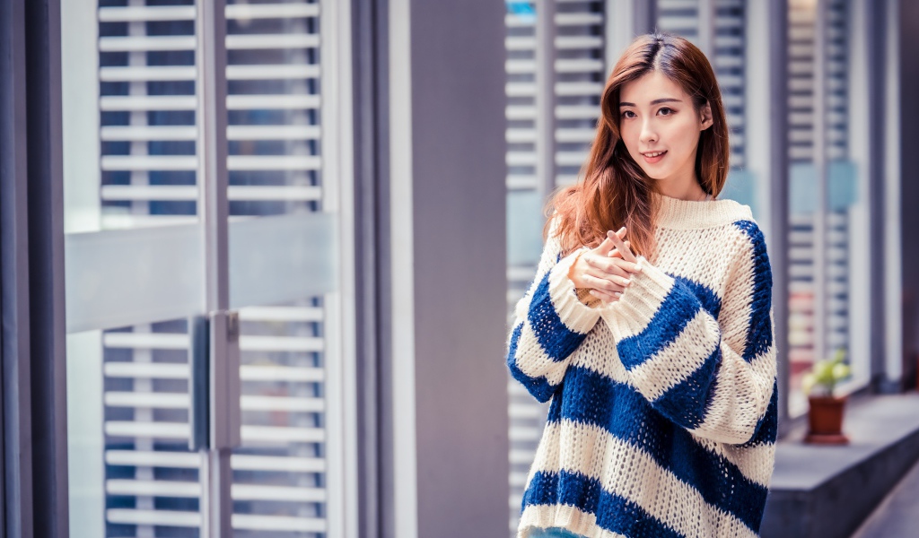 Девушка азиатка в теплом свитере стоит у окна