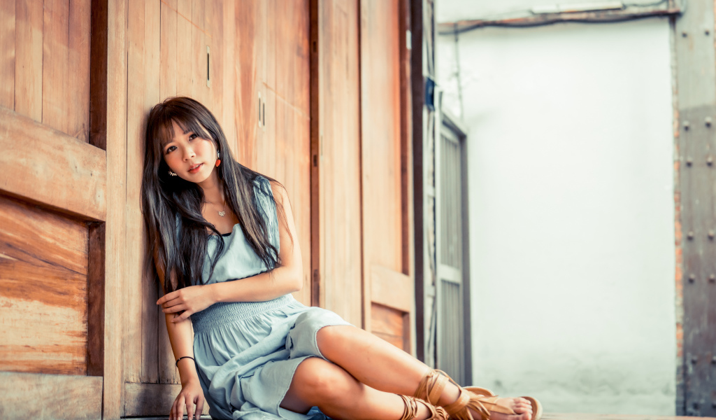 Девушка азиатка в платье сидит на полу у стены 