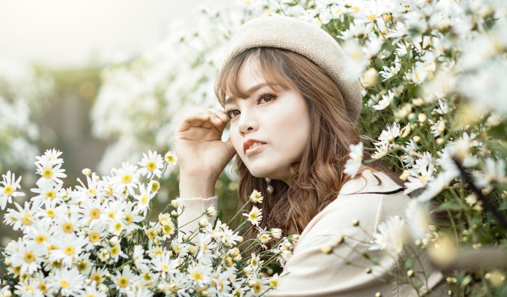 Девушка азиатка сидит в белых цветах ромашки 