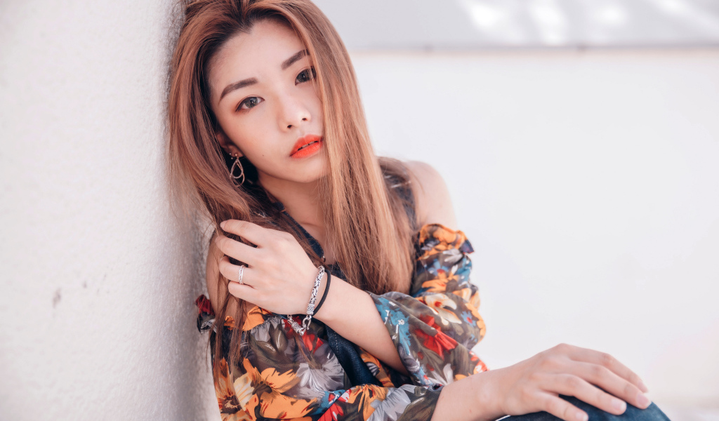 Девушка азиатка сидит на полу у стены 