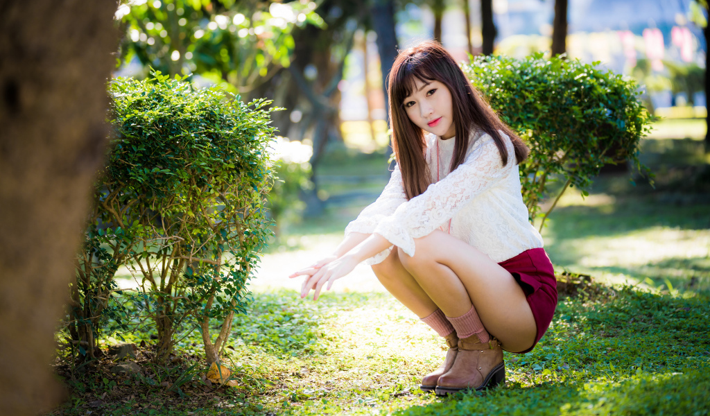 Девушка азиатка сидит на корточках в парке