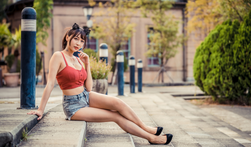 Азиатка в шортах сидит на ступенях 