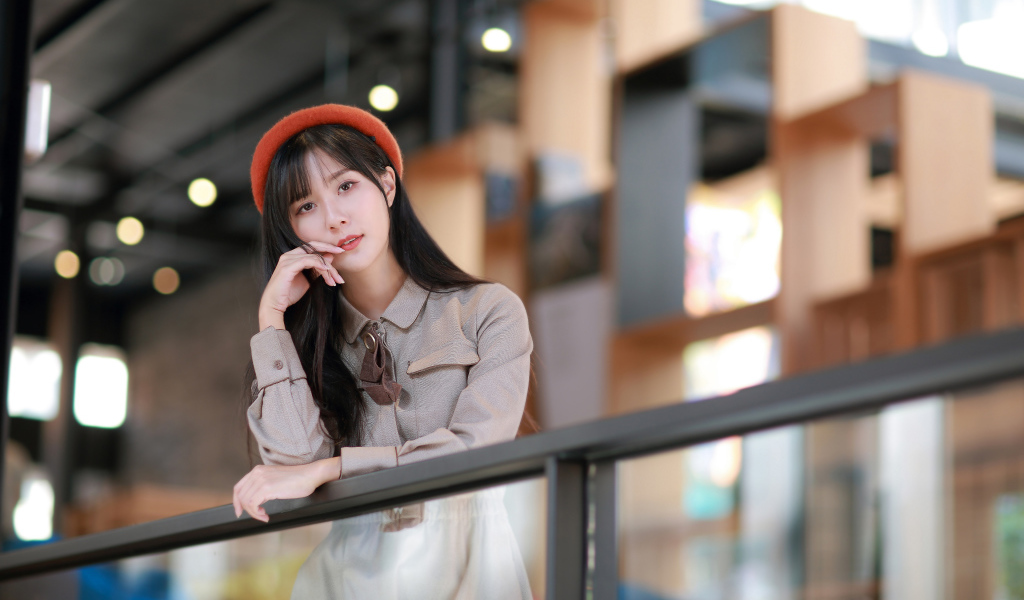 Азиатка в сером платье стоит у перил 