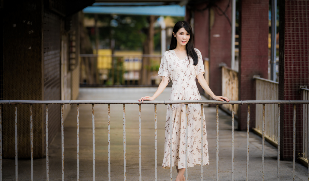 Красивая азиатка в платье стоит у перил