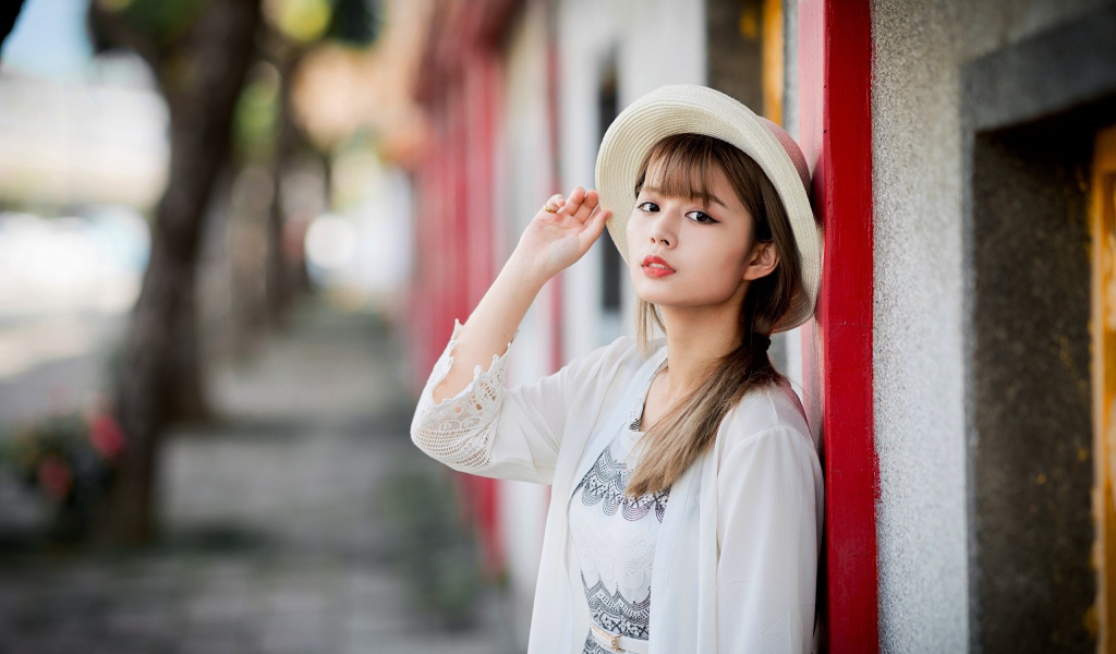 Красивая азиатка в шляпе стоит у стены