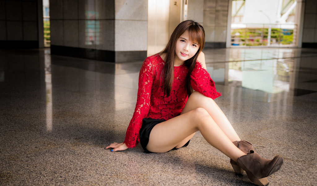Красивая девушка азиатка в красной блузке сидит на полу