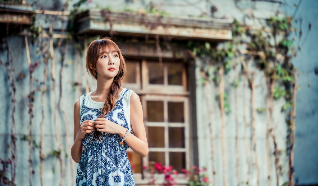 Красивая девушка азиатка в сарафане у старого дома 