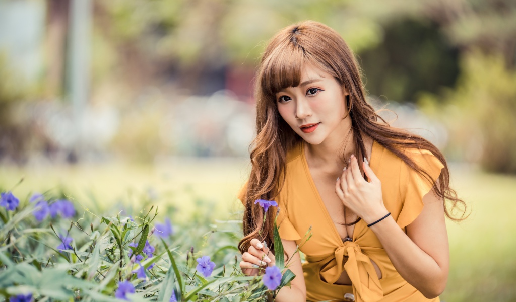 Красивая девушка азиатка в желтом платье у фиолетовых цветов 