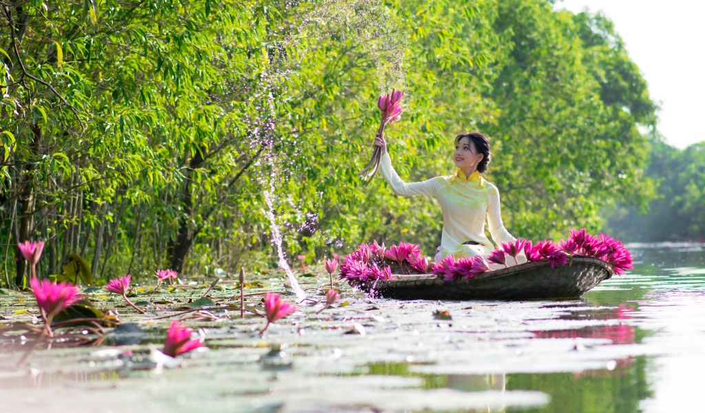 Красивая девушка азиатка на лодке рвет цветы лотоса в реке