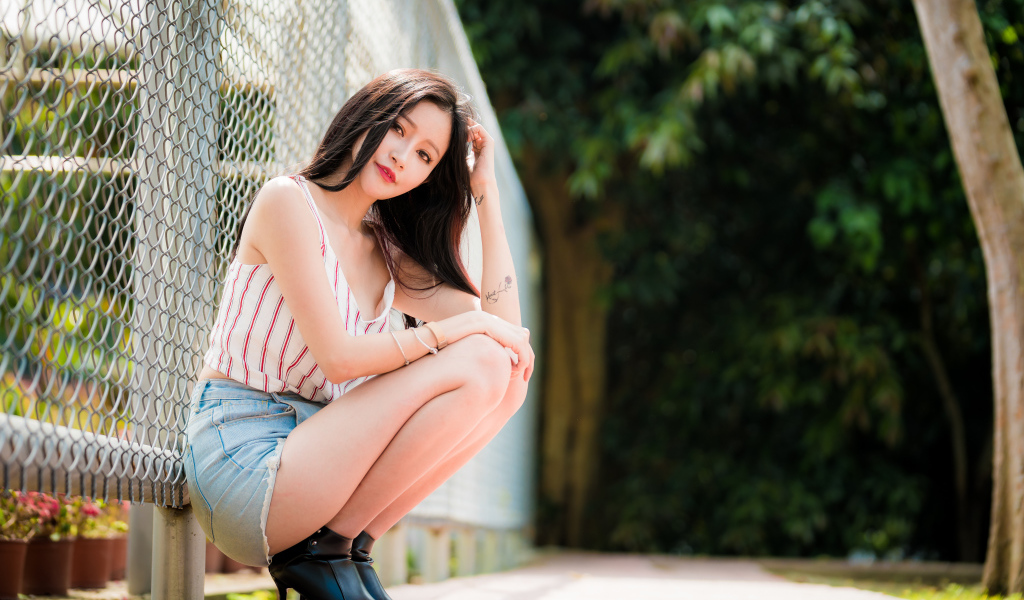 Красивая девушка азиатка сидит у железной сетки