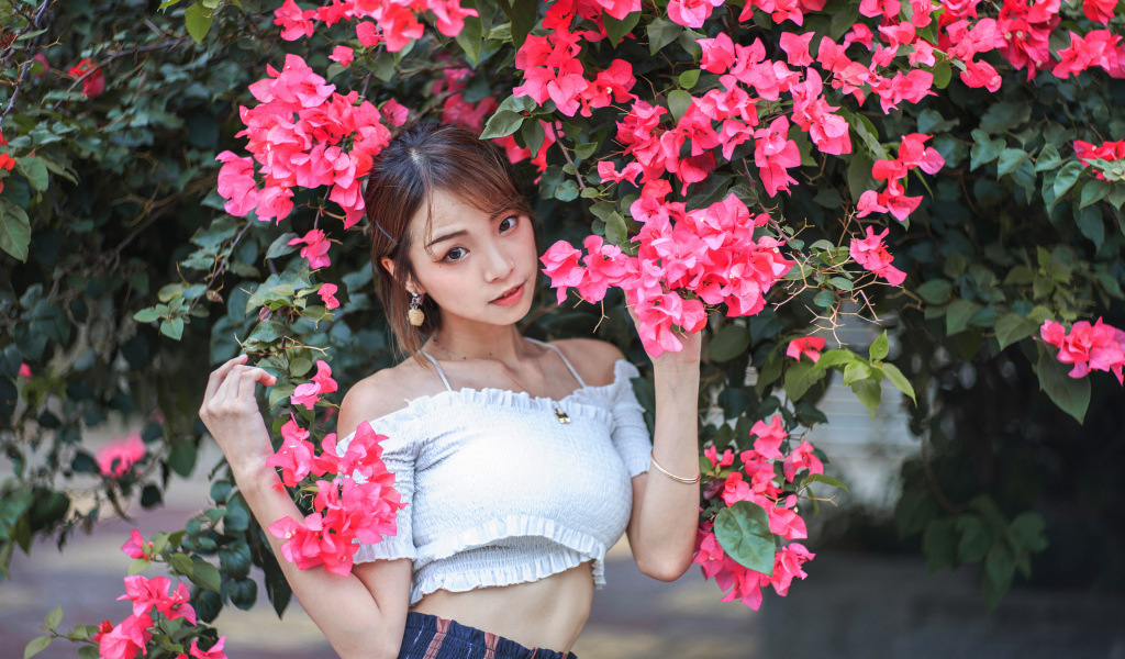 Красивая азиатка стоит у дерева с красными цветами