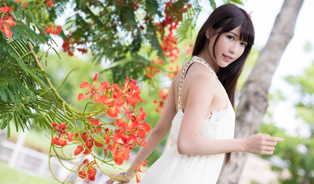 Beautiful asian girl in a red dress near a tree with flowers
