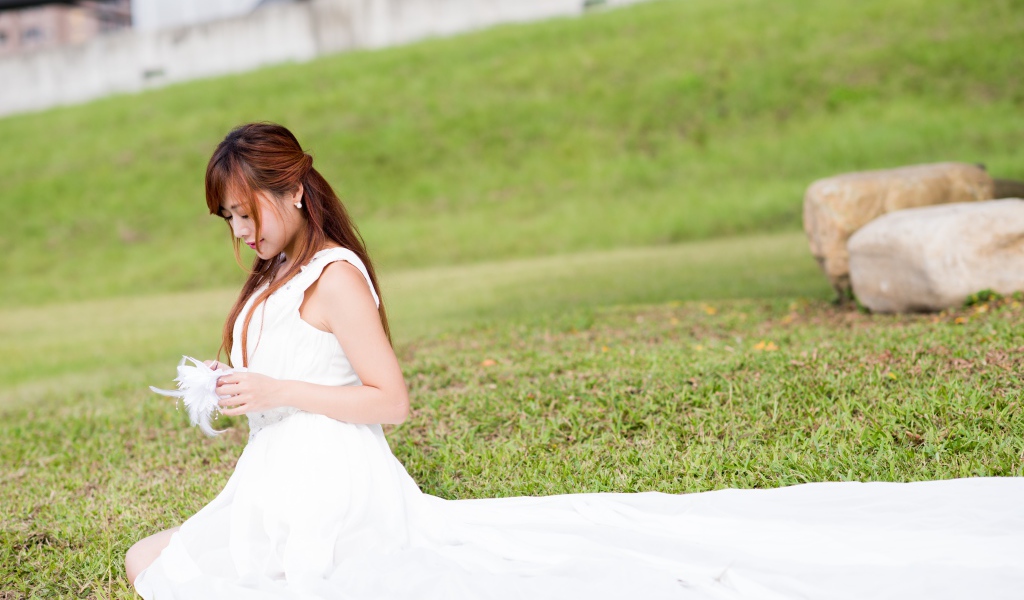 Красивая девушка азиатка в свадебном платье сидит на траве