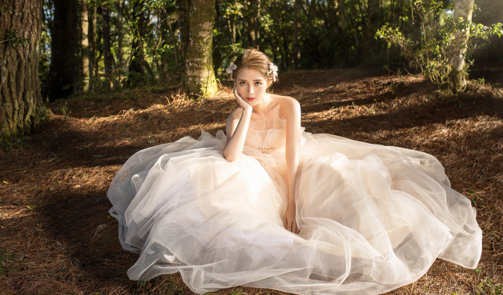 Красивая девушка азиатка в белом свадебном платье сидит на земле