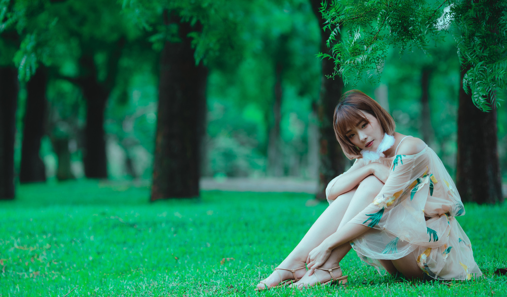 Красивая девушка азиатка сидит на зеленой траве в парке 