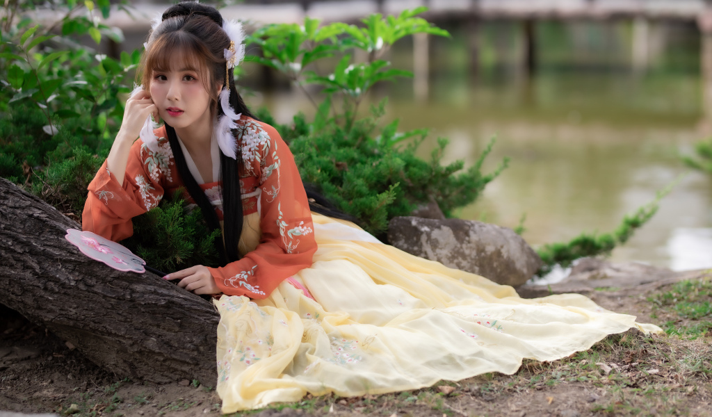 Красивая девушка азиатка сидит на земле у дерева 