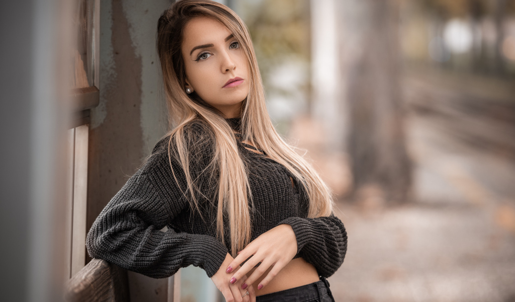 Красивая блондинка в вязаном свитере у стены 