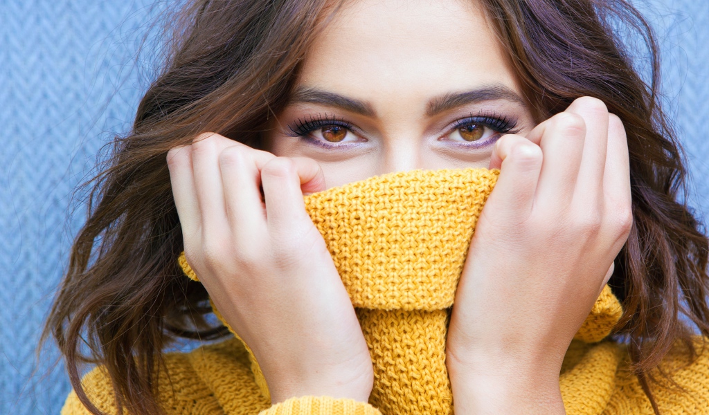 Красивая кареглазая девушка закрывает лицо свитером