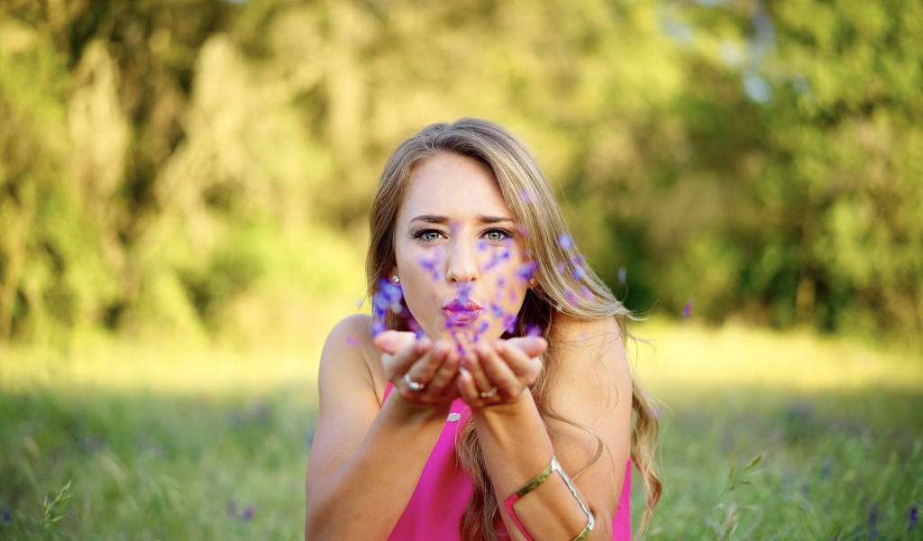 Красивая девушка сдувает лепестки с ладоней 