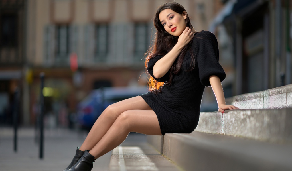 Красивая девушка в черном платье сидит на ступенях