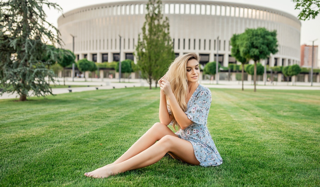 Красивая девушка в платье сидит на зеленом газоне 