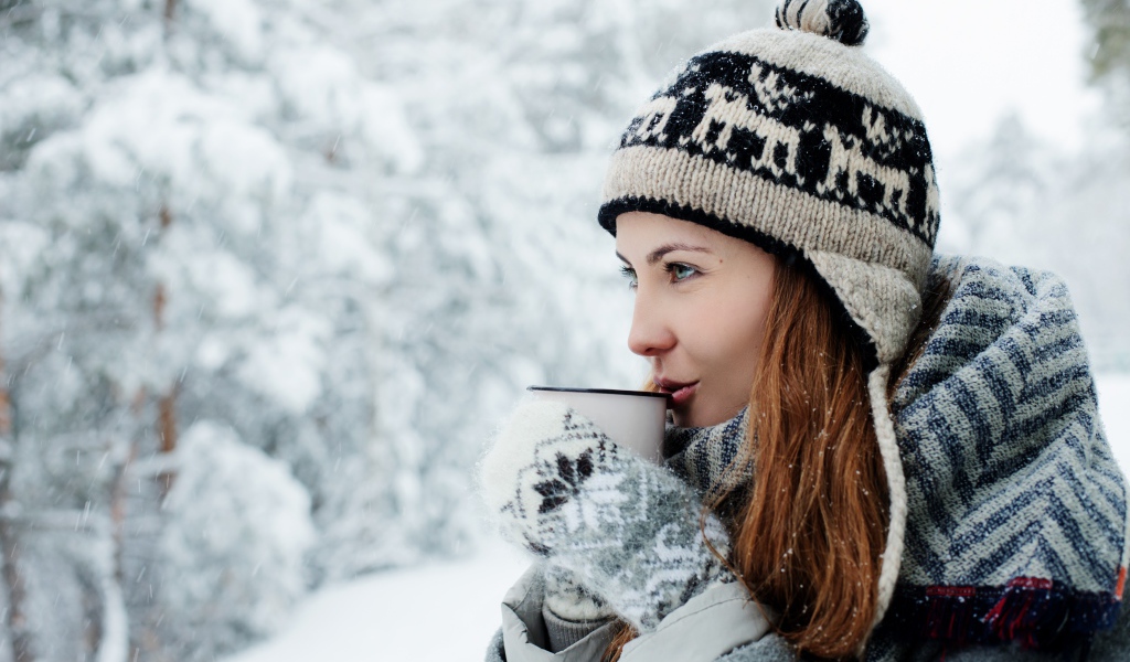 Красивая девушка в теплой шапке пьет кофе зимой на улице 