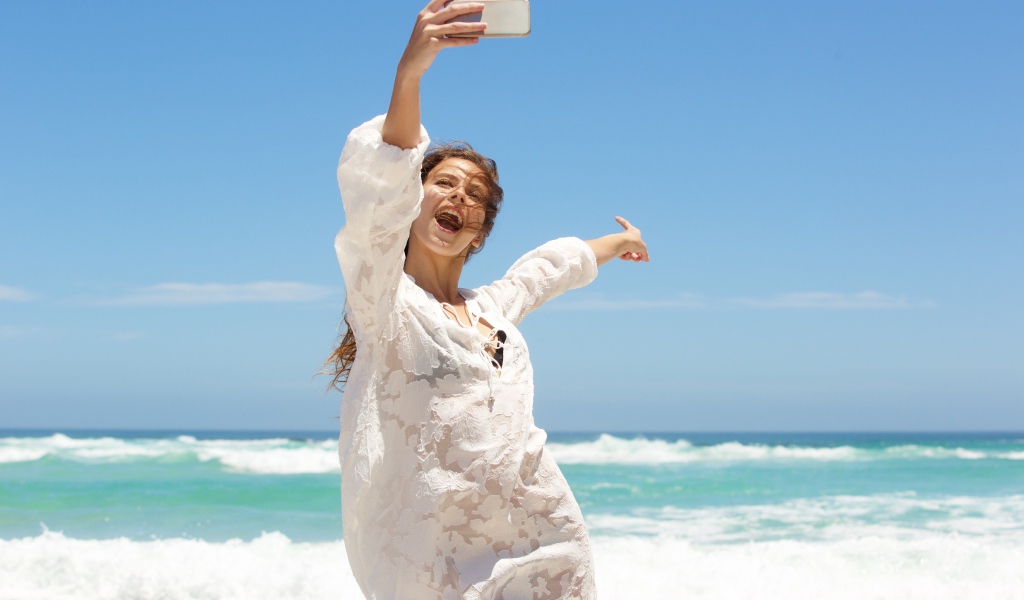 Красивая девушка в белом платье делает селфи на море 