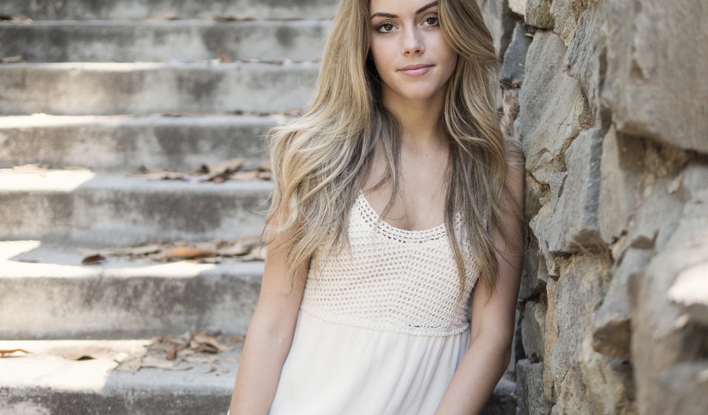 Красивая девушка в белом платье у каменной стены 