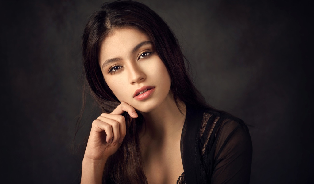 Красивая девушка в черном сидит на сером фоне