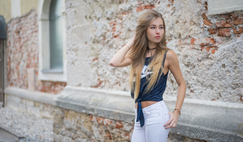 Красивая девушка в белых брюках стоит у стены 