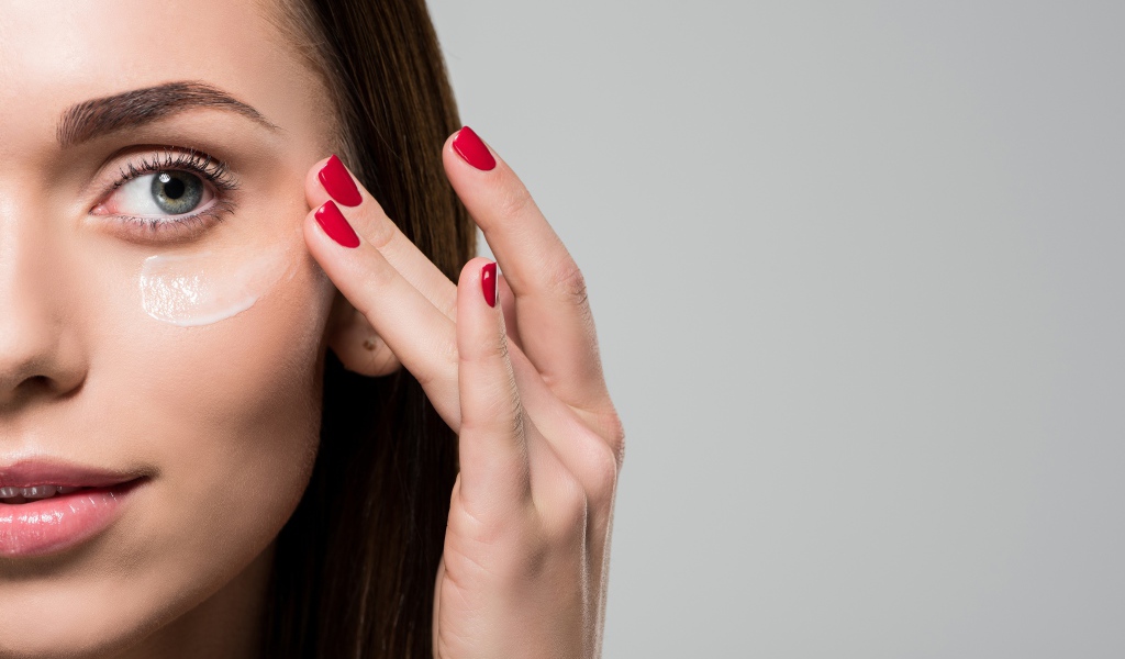 Красивая девушка модель мажет лицо кремом на сером фоне 