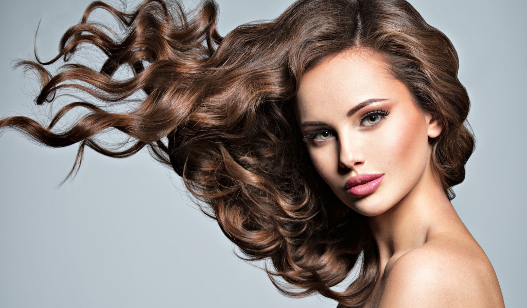 Красивая девушка модель с волнистыми волосами на сером фоне