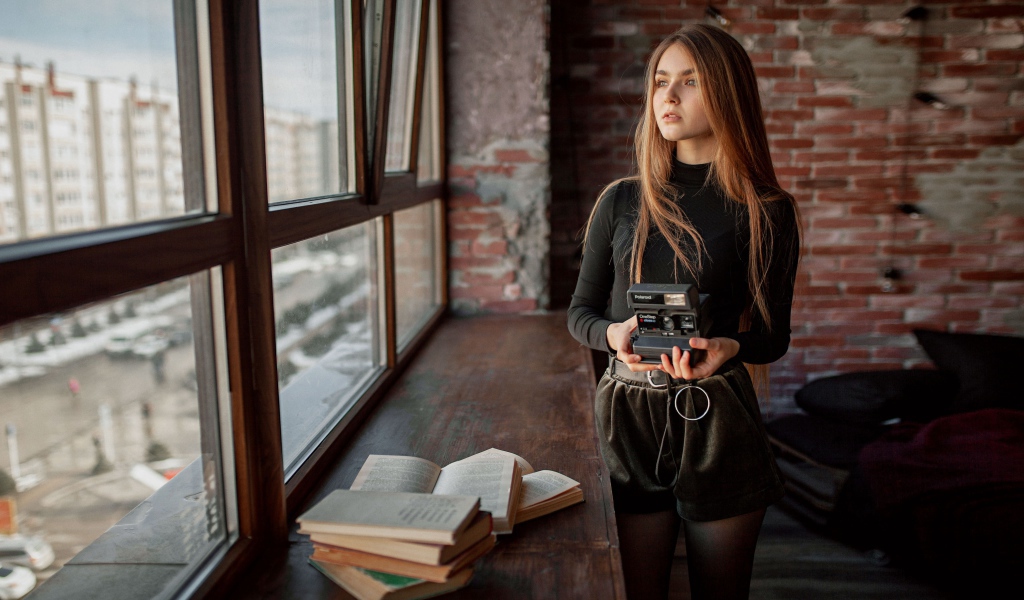 Красивая девушка с фотоаппаратом в руках у окна 
