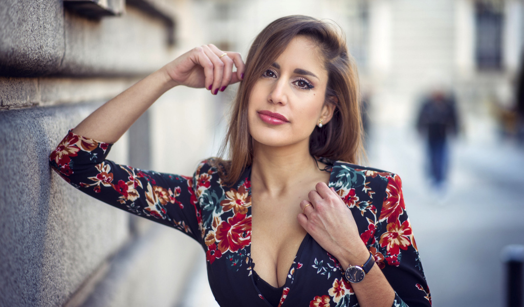 Красивая девушка с часами на руке стоит у стены