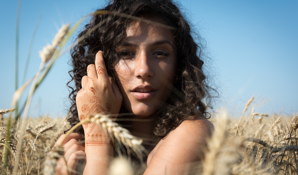 Красивая девушка с рисунком мехенди на руке на пшеничном поле 