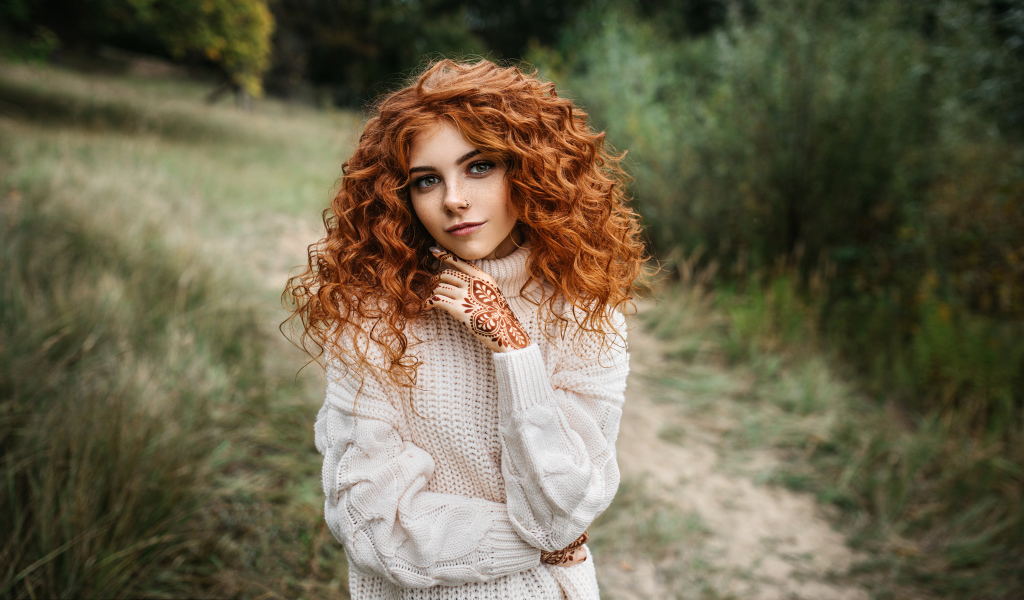Красивая рыжеволосая девушка в белом свитере с рисунками из хны на руках