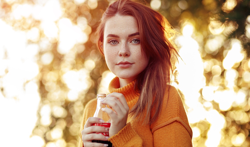 Красивая рыжеволосая девушка с бутылкой кока колы в руке 