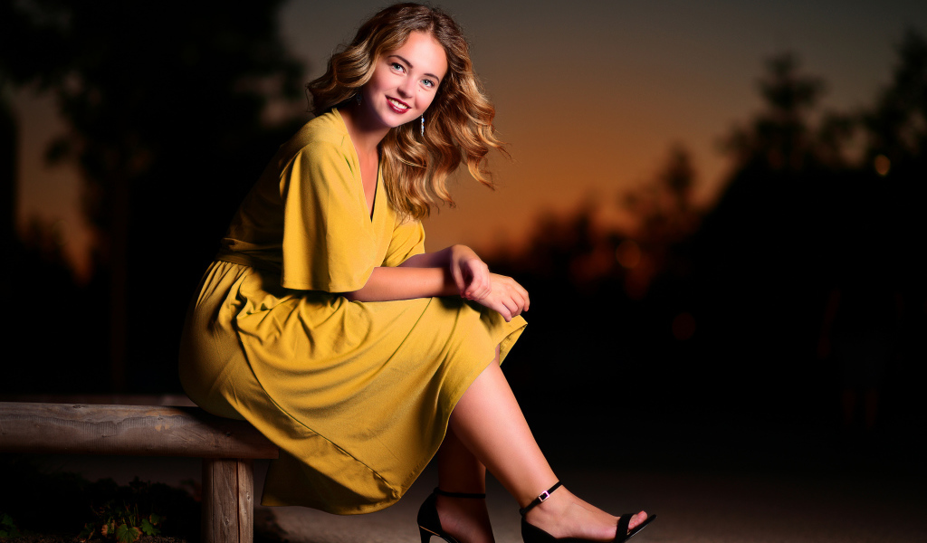 Красивая улыбающаяся девушка в желтом платье сидит на лавке 