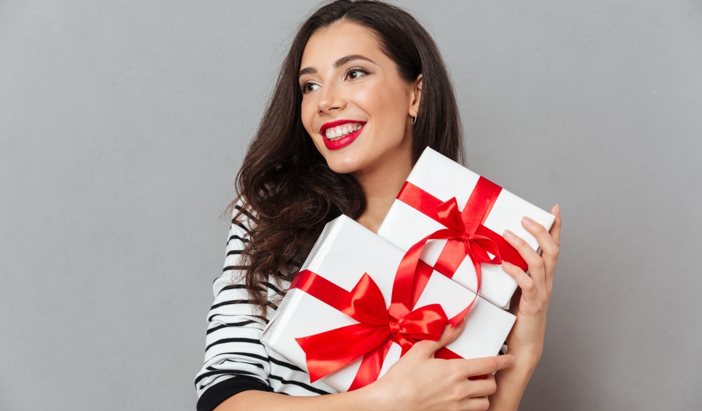 Красивая улыбающаяся девушка с подарками в руках на сером фоне 