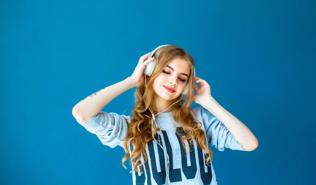 Красивая молодая девушка в наушниках на голубом фоне