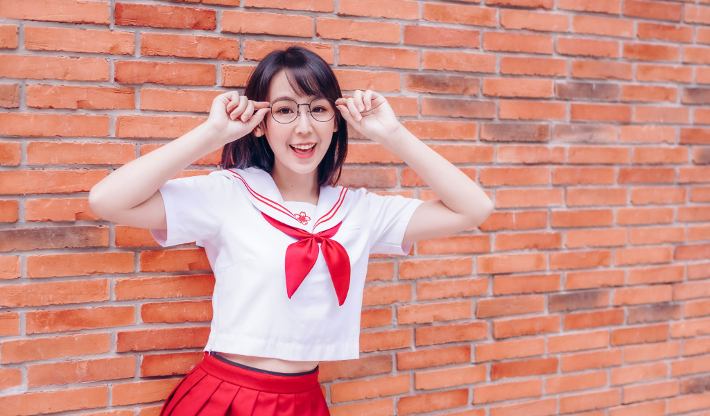 Яркая веселая азиатка в очках у кирпичной стены