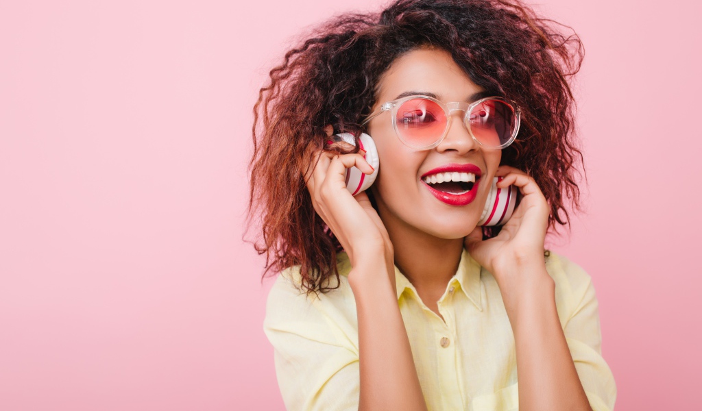Яркая улыбающаяся девушка слушает музыку в наушниках 