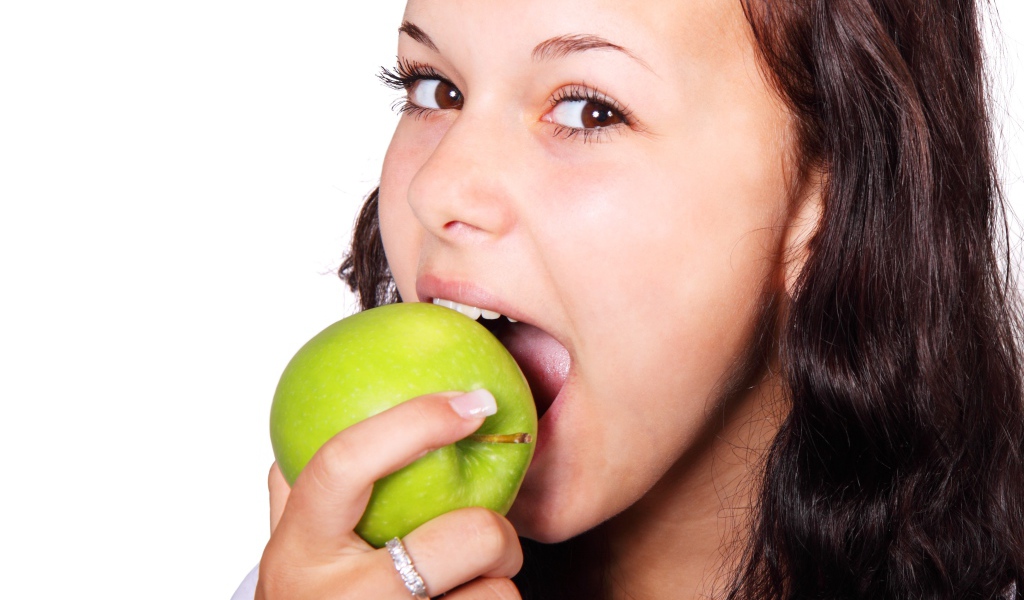 Кареглазая девушка ест зеленое яблоко