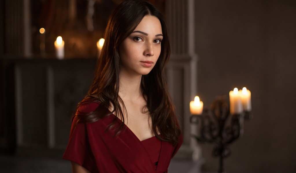 Кареглазая девушка в красном платье в комнате со свечами