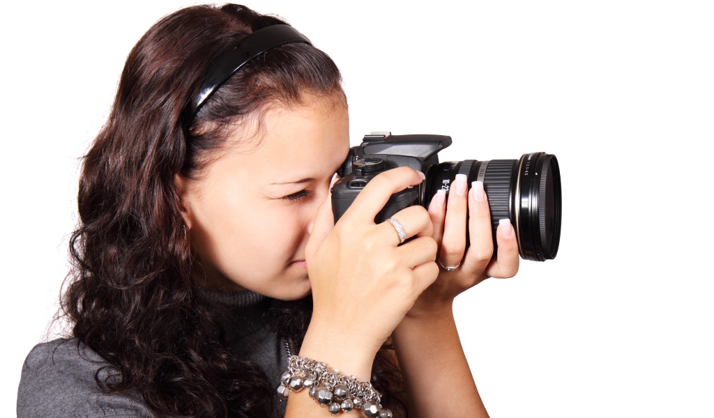 Молодая девушка шатенка с фотоаппаратом в руках на белом фоне