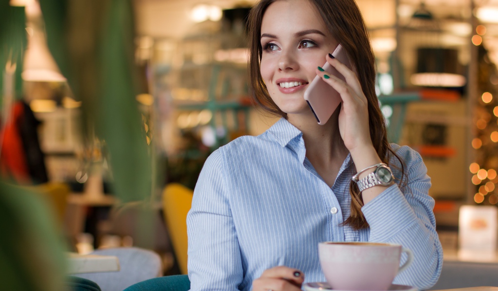 Деловая девушка в рубашке разговаривает в кафе по телефону