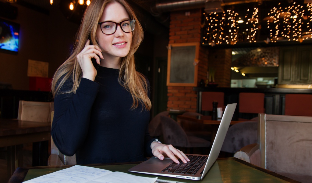 Деловая девушка в очках сидит с кафе с ноутбуком