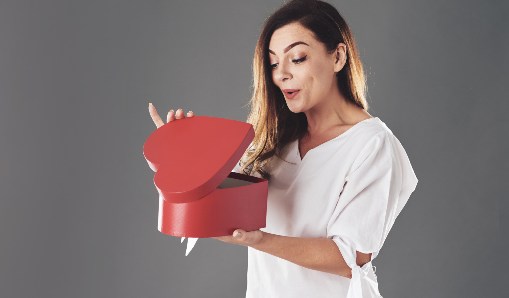 Любопытная девушка смотрит в красную коробку в форме сердца