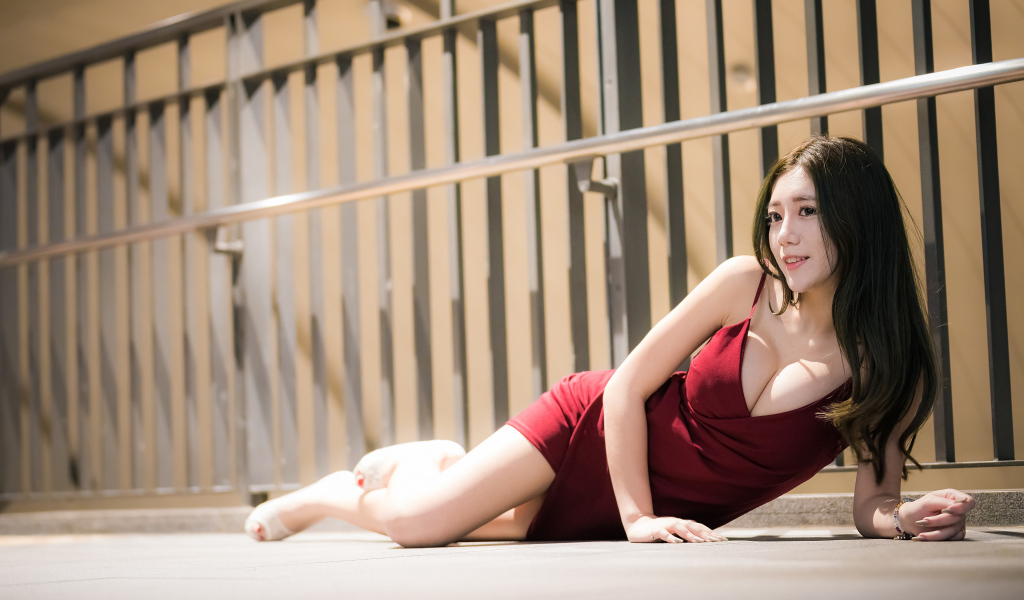 Милая девушка азиатка в красном платье лежит на земле